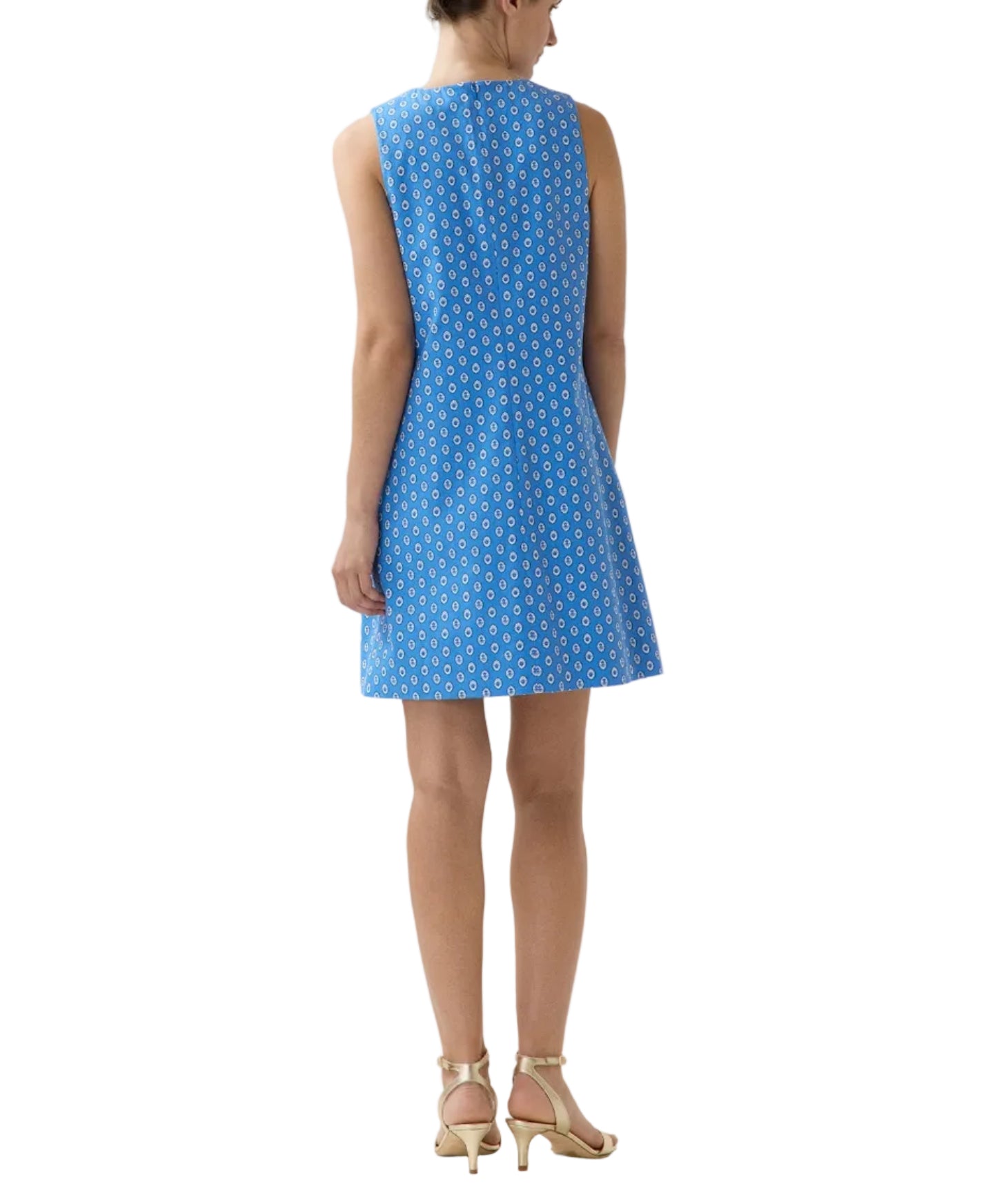 Woman shown from the back wearing the Ann Mashburn Susy Shift Dress—a sleeveless, knee-length blue dress with a white geometric pattern in a 1960s A-line silhouette—paired with beige heeled sandals.