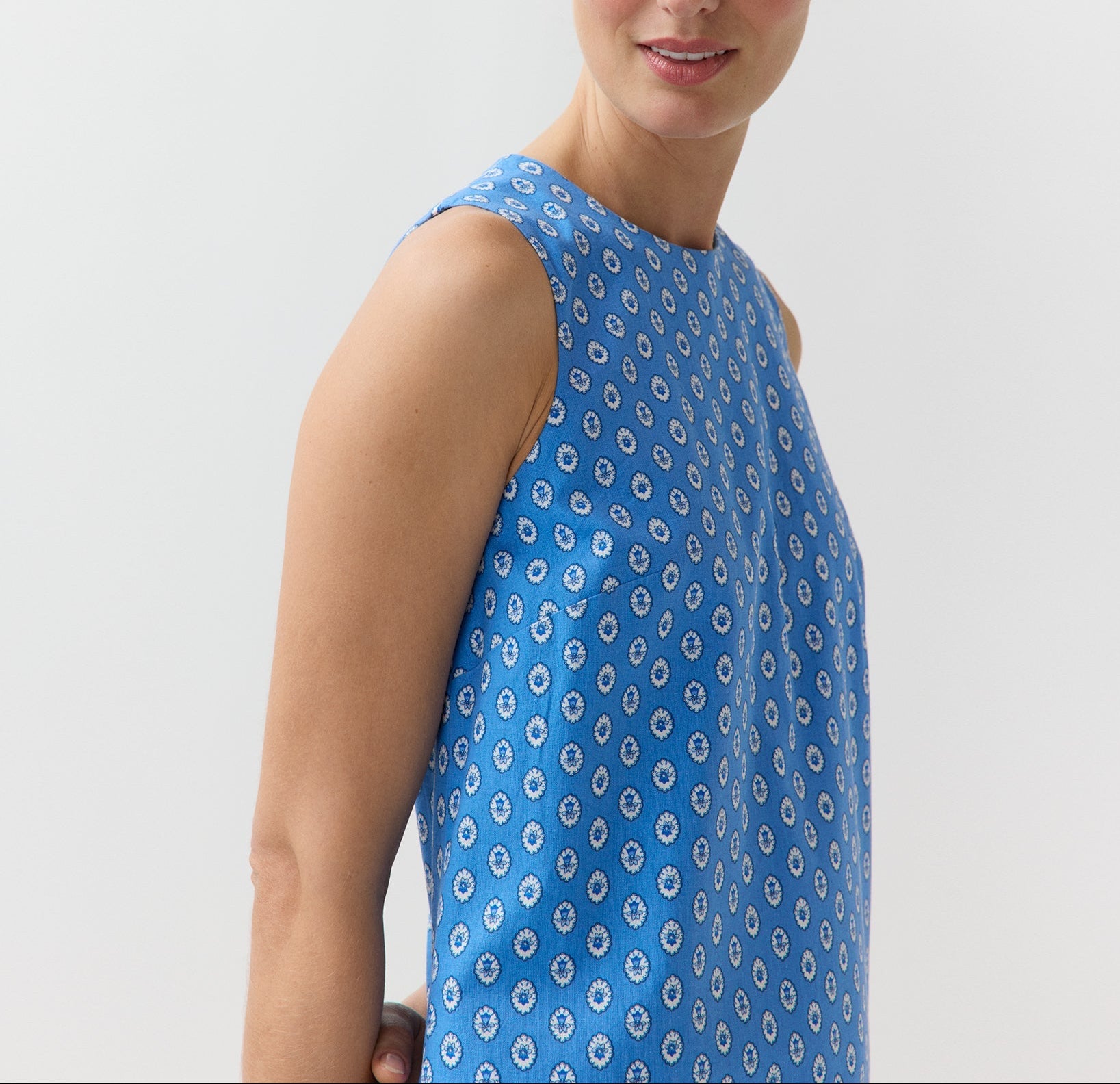 A woman models the Ann Mashburn Susy Shift Dress—a sleeveless, blue 1960s-style A-line dress with a white circular pattern in Japanese compact cotton—against a plain light background.