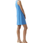 A woman in profile wears the Ann Mashburn Susy Shift Dress, a sleeveless blue compact cotton A-line style, with beige heeled sandals, posed against a plain white background.