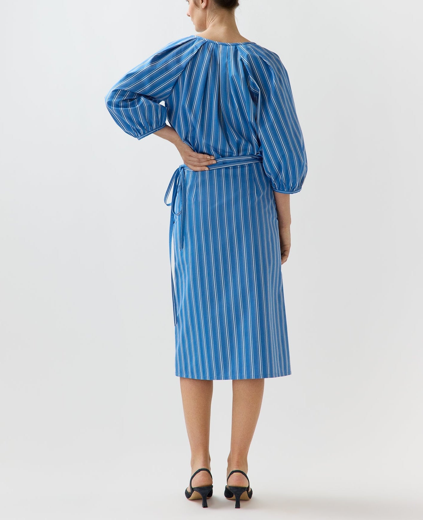 A woman stands facing away, wearing the Ann Mashburn Morgan Variegated Stripe Skirt with black heeled sandals.