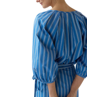 A person is shown from behind, hands back, wearing the Ann Mashburn Victoria Variegated Stripe Blouse in blue and white stripes, set against a crisp white background.