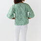 A person stands facing away, wearing the Elora Volume Liberty Top by Ann Mashburn—featuring a green and white zebra print with loose sleeves—and white pants, set against a plain white background.