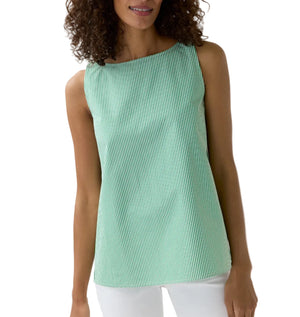 A woman wears the Ann Mashburn Bell Top, a sleeveless green-and-white Italian striped poplin blouse, paired with white pants and standing against a plain white background.