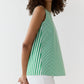 A woman wears the Ann Mashburn Bell Top—a simple tank in Italian striped poplin with green and white vertical stripes and a bateau neckline—paired with white pants, set against a plain white background.