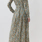 A person stands with their back to the camera, wearing the Ann Mashburn Classic Shirtwaist Rachel Liberty Dress—an ankle-length, long-sleeve floral dress—paired with brown ankle boots against a plain light background.