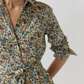 An Ann Mashburn Classic Shirtwaist Rachel Liberty Dress, featuring a collared neckline and long sleeves, showcases a blue, green, and brown floral print crafted from Liberty Fabrics and is finished with a matching belt tied at the waist.