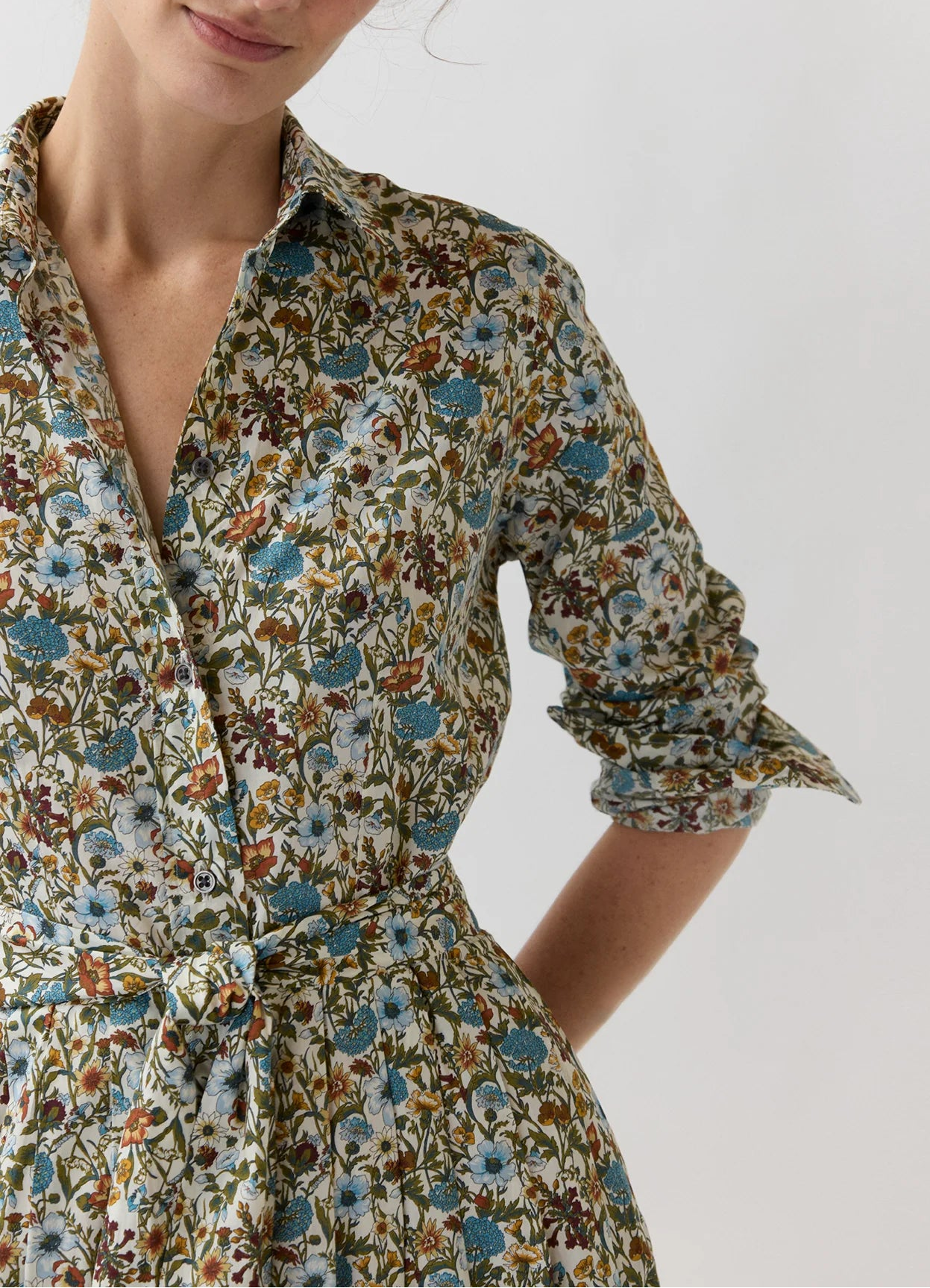 An Ann Mashburn Classic Shirtwaist Rachel Liberty Dress, featuring a collared neckline and long sleeves, showcases a blue, green, and brown floral print crafted from Liberty Fabrics and is finished with a matching belt tied at the waist.