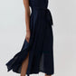 A woman is wearing the Ann Mashburn Scarlett Silk Georgette Dress—a sleeveless, navy blue midi dress with a waist tie—paired with black heeled sandals, standing against a plain light background. This lightweight dress from Ann Mashburn drapes beautifully, offering effortless style and elegance.