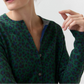 A person wearing the Ann Mashburn Rosie Cotton Silk Leopard Cardigan—featuring a green and blue leopard print in a stretchy knit—with the top buttons undone, facing slightly away from the camera.
