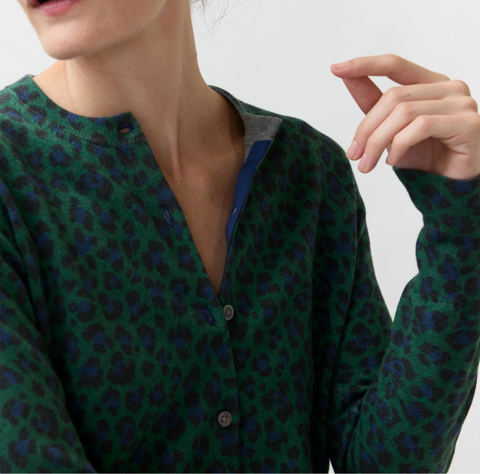 A person wearing the Ann Mashburn Rosie Cotton Silk Leopard Cardigan—featuring a green and blue leopard print in a stretchy knit—with the top buttons undone, facing slightly away from the camera.