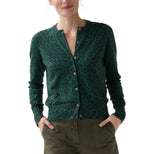An Ann Mashburn Rosie Cotton Silk Leopard Cardigan in green and black is worn with olive green pants, as the woman stands with her hands in her pockets.