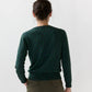 A person with dark hair in a bun, wearing the Ann Mashburn Rosie Cotton Silk Leopard Cardigan and olive pants, is shown from the back against a plain light background.