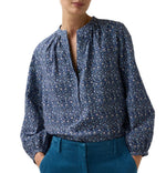 The Ann Mashburn Sienna Crinkle Cotton Top is a long-sleeved, blue floral print blouse in Japanese crinkle cotton, featuring a split neckline, romantic sleeves, and gathered shoulders.