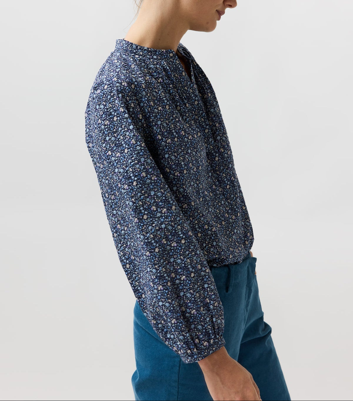 A woman wearing the Sienna Crinkle Cotton Top, a billowy, navy blue floral print blouse with romantic sleeves and a split neckline, paired with teal trousers.