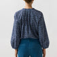 Back view of a person wearing a navy blue billowy Sienna Crinkle Cotton Top with a small floral pattern and teal trousers.