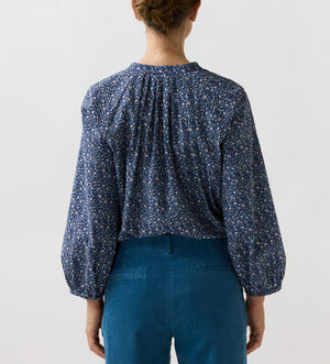 Back view of a person wearing a navy blue billowy Sienna Crinkle Cotton Top with a small floral pattern and teal trousers.