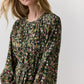 The Ann Mashburn Aba Silk Maxi Dress features a dark green botanical print with pink and white flowers, scrolling vines, a belt, and elasticated cuffs in a long-sleeved party silhouette.