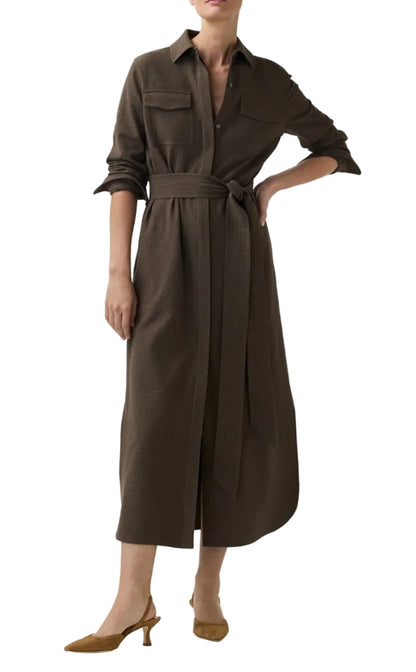A person wearing the Ann Mashburn Maude Crinkle Cotton/Wool Dress—a long-sleeve, belted brown midi shirt dress with a collar and pockets made from textured fabric—stands with one hand on their hip and pairs the look with tan heeled shoes.