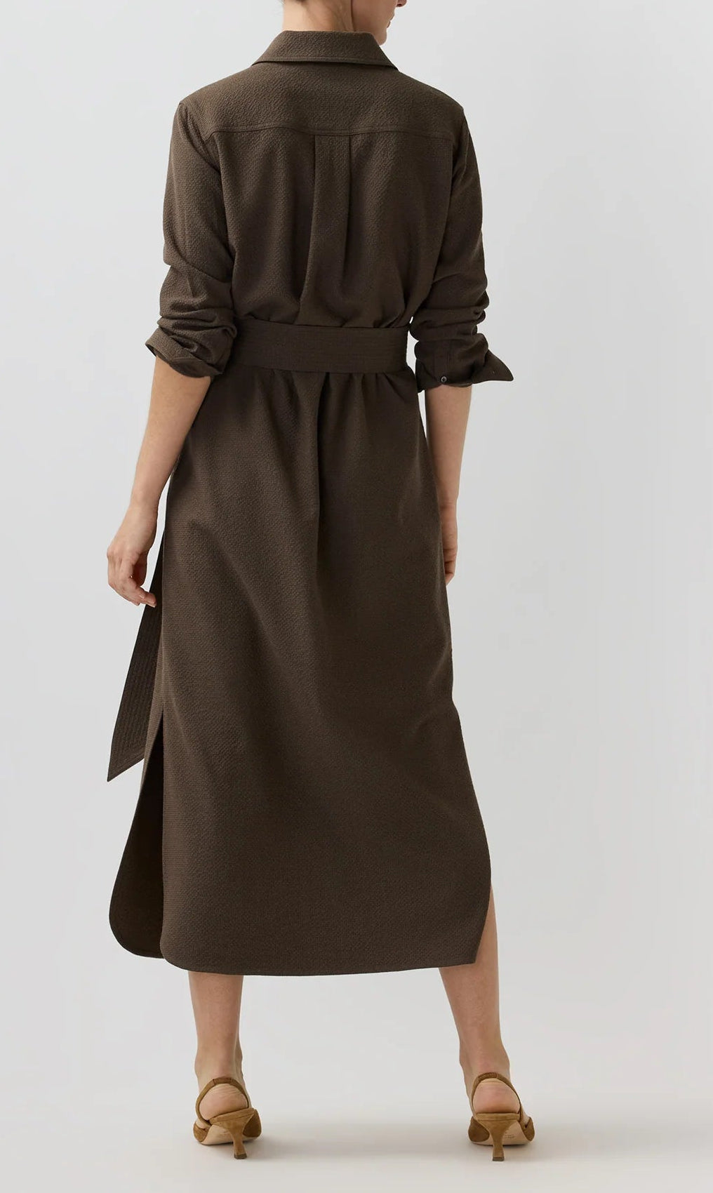 A person stands with their back to the camera, wearing the Ann Mashburn Maude Crinkle Cotton/Wool Dress in brown, styled with beige heeled sandals against a plain light background.