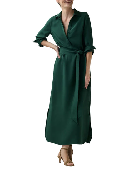 A person wearing a dark green Piper Silk Crepe Maxi Dress with a collared, tie-waist design and brown heeled sandals.