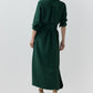 Back view of a person wearing a dark green Piper Silk Crepe Maxi Dress with a collar and waist tie, paired with tan heeled sandals.