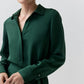 A person wearing a dark green Piper Silk Crepe Maxi Dress in a lightweight crepe de chine with a collared V-neck, long sleeves, and buttoned cuffs.