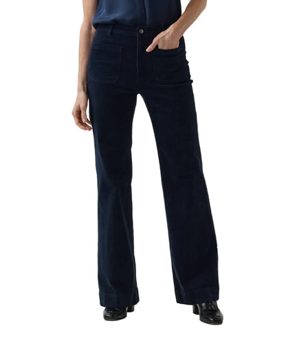 A person wearing Ann Mashburn Camille Patch-Pocket Stretch Corduroy Jean in dark blue with front patch pockets and black loafers.