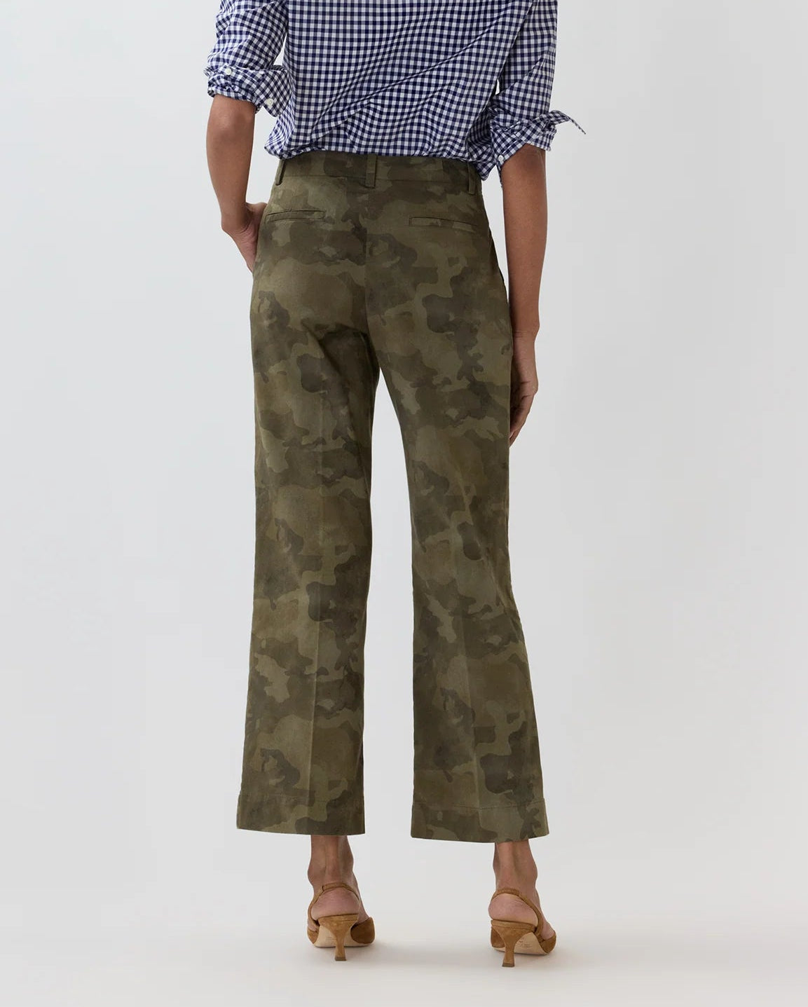 A person wearing the Ann Mashburn Frankie Stretch Twill Cropped Pant in green camouflage, featuring a barely-there waistband, paired with a blue and white checkered blouse and tan heeled sandals, stands against a plain light background with their back to the camera.