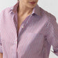 A person is wearing the Ann Mashburn Sidney Banker Stripe Poplin Shirt, a red and white vertically striped button-up made from Italian poplin with a spread collar and rolled-up sleeves, shown from the shoulders to the waist against a plain background.