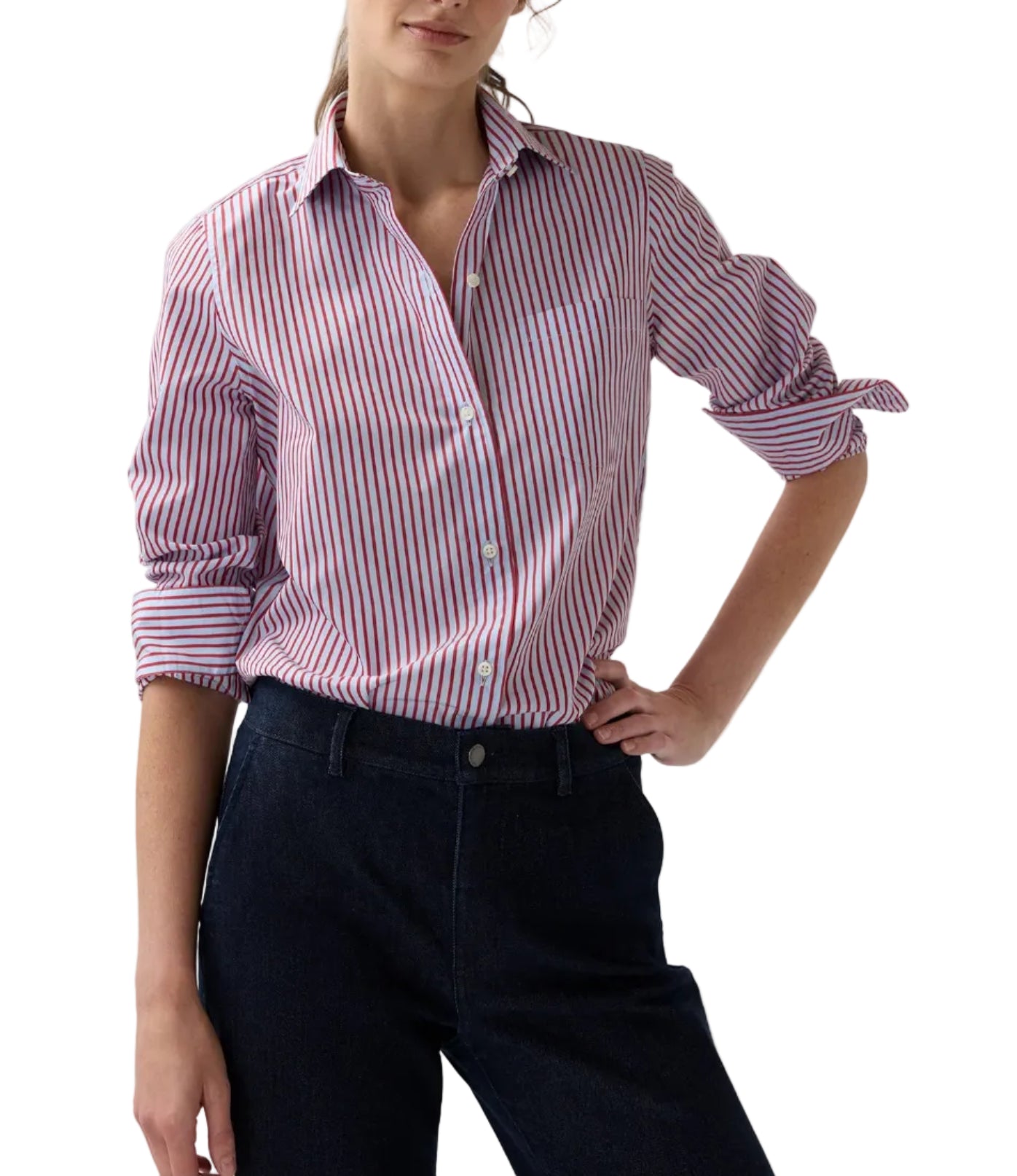 Wearing the Sidney Banker Stripe Poplin Shirt by Ann Mashburn—a red and white menswear stripe button-up crafted from Italian poplin with a spread collar—this person has the sleeves rolled up and pairs it with dark pants, standing with one hand on hip.
