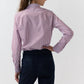 A person stands with their back to the camera, wearing the Ann Mashburn Sidney Banker Stripe Poplin Shirt—a red and white menswear stripe button-down crafted from fine Italian poplin—paired with dark blue jeans, set against a plain light background.