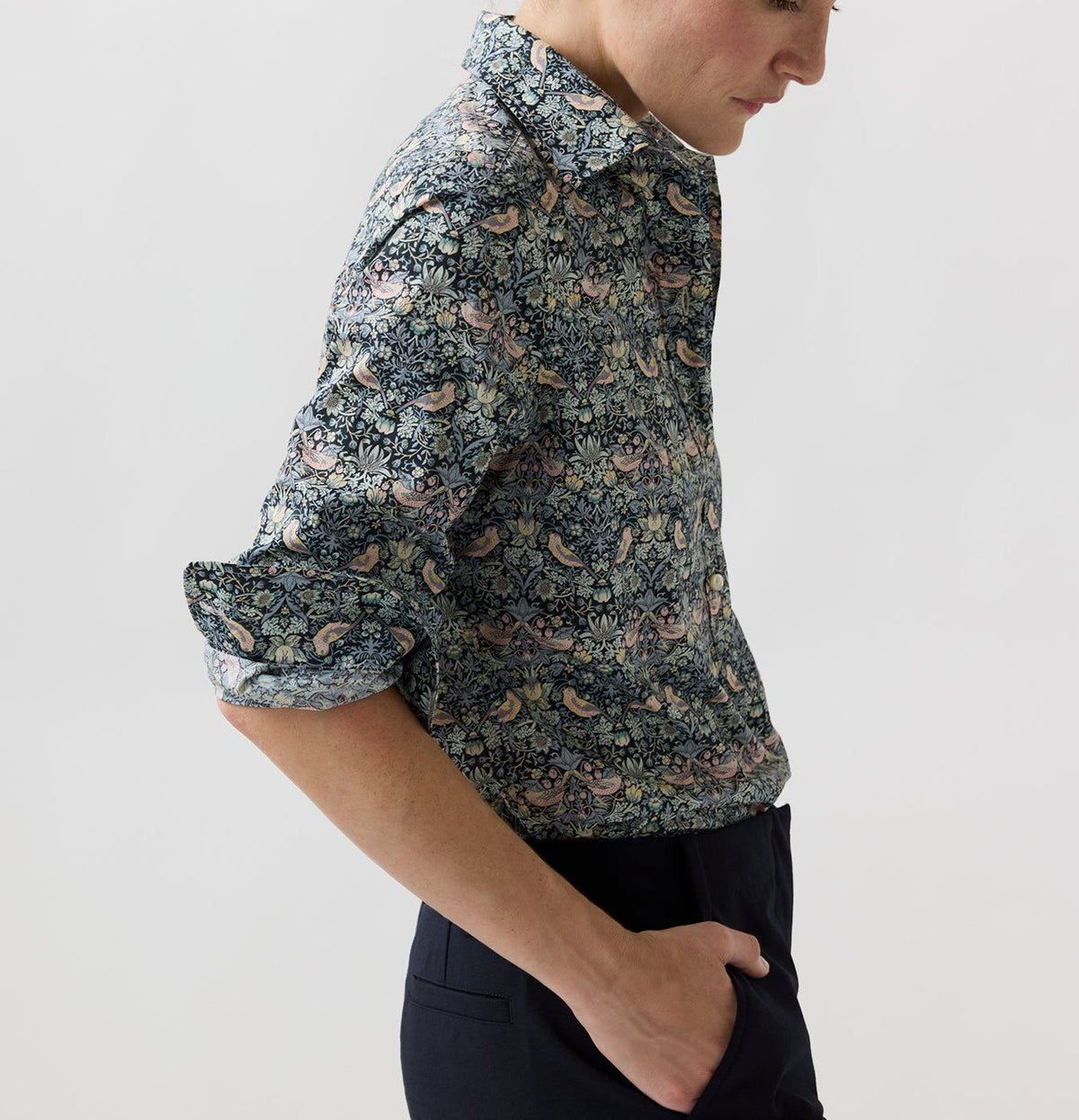 A person wearing an Ann Mashburn Tomboy Popover Liberty Shirt with a dark floral and bird print, featuring rolled-up sleeves and a relaxed fit.