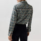 Back view of a person in an Ann Mashburn Tomboy Popover Liberty Shirt with a multicolored floral and bird pattern, tucked into black trousers.