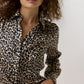 A person wears an Ann Mashburn Natalia Silk Blouse in a classic long-sleeved button-up style with an Italian charmeuse leopard print pattern.