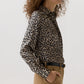 Ann Mashburn Natalia Silk Blouse in a tan and black leopard print, tucked into tan trousers with a black belt.