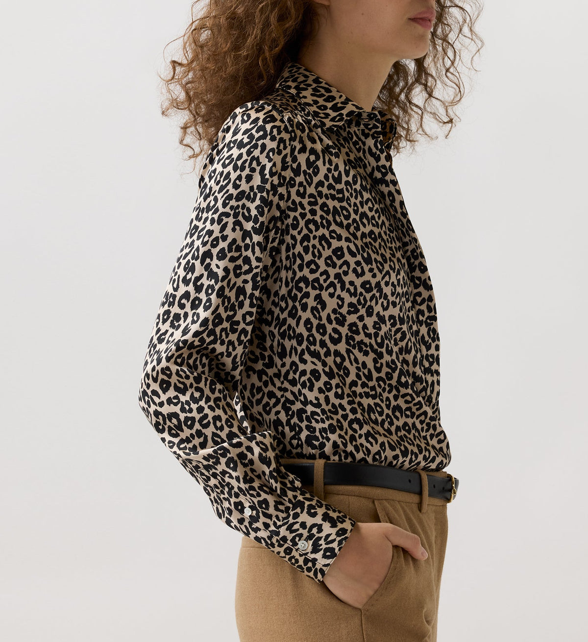 Ann Mashburn Natalia Silk Blouse in a tan and black leopard print, tucked into tan trousers with a black belt.
