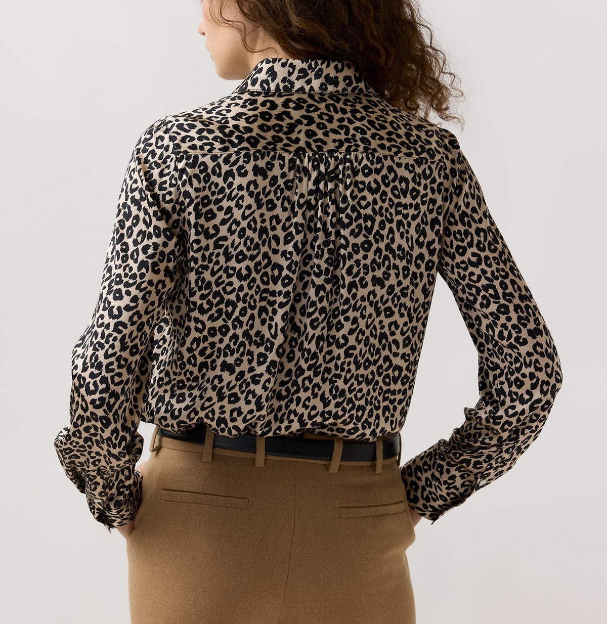 Back view of an Ann Mashburn Natalia Silk Blouse in a classic leopard print, tucked into tan trousers with a black belt.