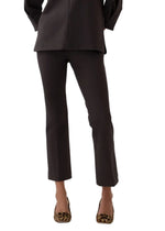 A person wearing the Ann Mashburn Faye Flare Cropped Pant, paired with a dark long top and leopard-print shoes, stands against a plain white background.
