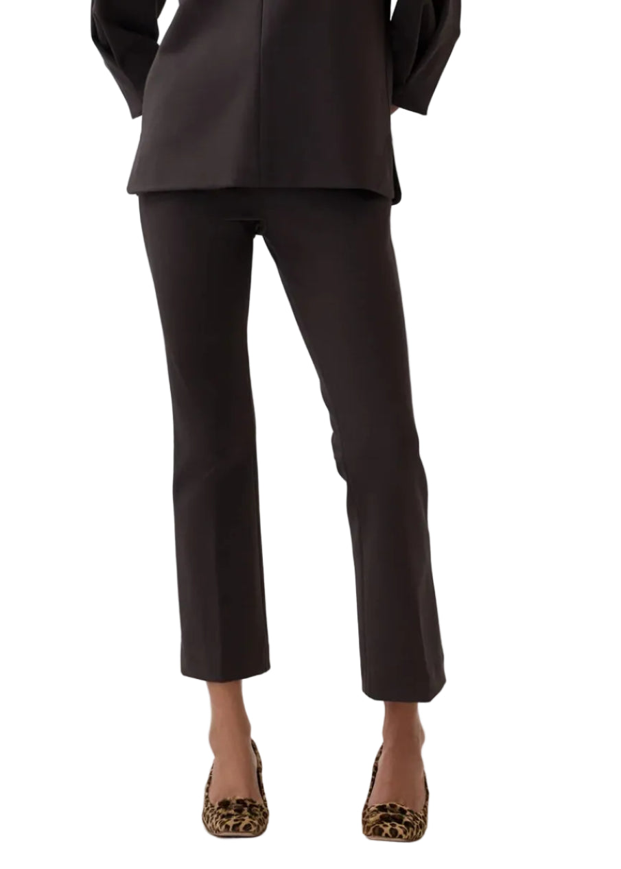 A person wearing the Ann Mashburn Faye Flare Cropped Pant, paired with a dark long top and leopard-print shoes, stands against a plain white background.