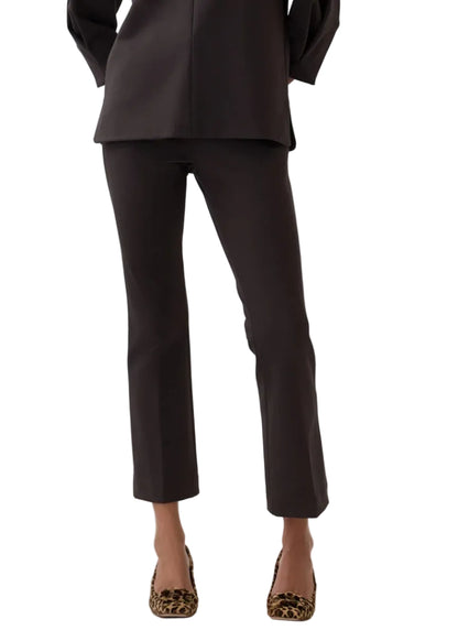 A person wearing the Ann Mashburn Faye Flare Cropped Pant, paired with a dark long top and leopard-print shoes, stands against a plain white background.