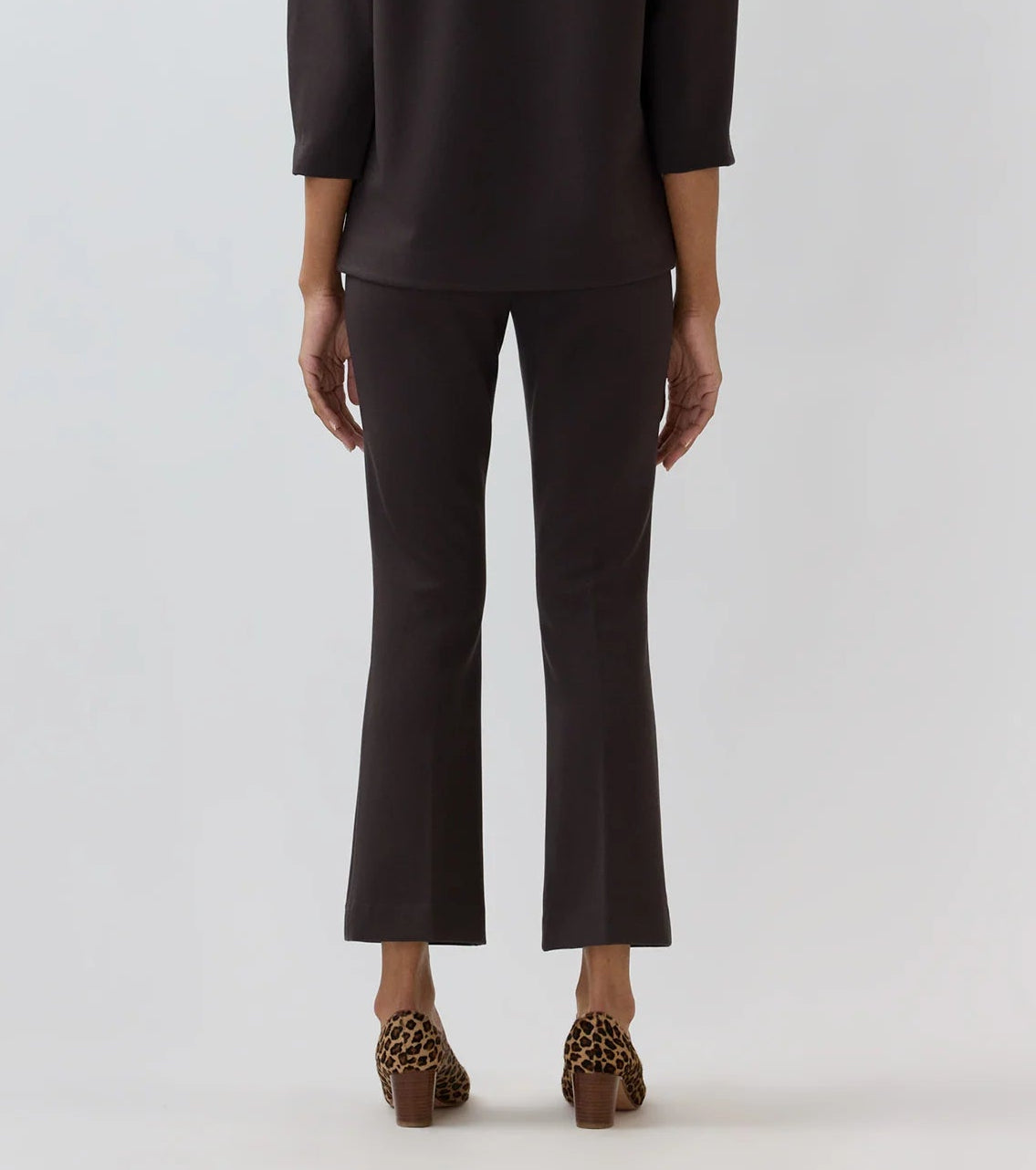 A person stands facing away against a plain background, wearing the Ann Mashburn Faye Flare Cropped Pant and a matching three-quarter sleeve top, paired with brown leopard-print heeled shoes.
