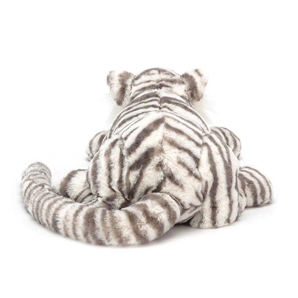 A Jellycat Sacha Snow Tiger, Really Big plush toy is shown from the back, lying down with its tail curled to the side. The plush white tiger with black stripes exudes a serene, lifelike charm.