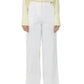 A person wearing Callas Milano Sailor Pants in white, paired with a pale yellow button-up shirt and black sandals, stands against a white background.