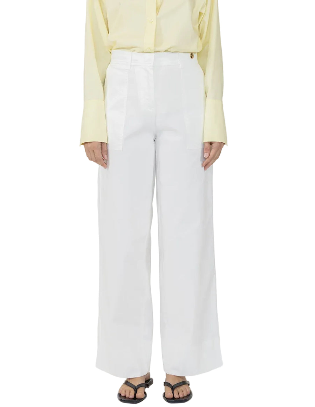 A person wearing Callas Milano Sailor Pants in white, paired with a pale yellow button-up shirt and black sandals, stands against a white background.