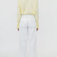 A person stands facing away, wearing Callas Milano’s Sailor Pant—a high-waisted, white wide leg pant in soft cotton twill—paired with a light yellow long-sleeve shirt against a plain white background.