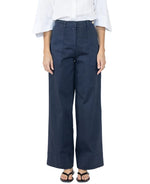 A person wearing a white blouse, black sandals, and Callas Milano Sailor Pant in navy cotton twill with front seams stands against a plain background.