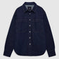 The Samy Shirt by Anine Bing, crafted from dark blue cotton denim canvas, features silver buttons, two spacious chest pockets, and a pointed collar; it is displayed laid flat on a plain light background.
