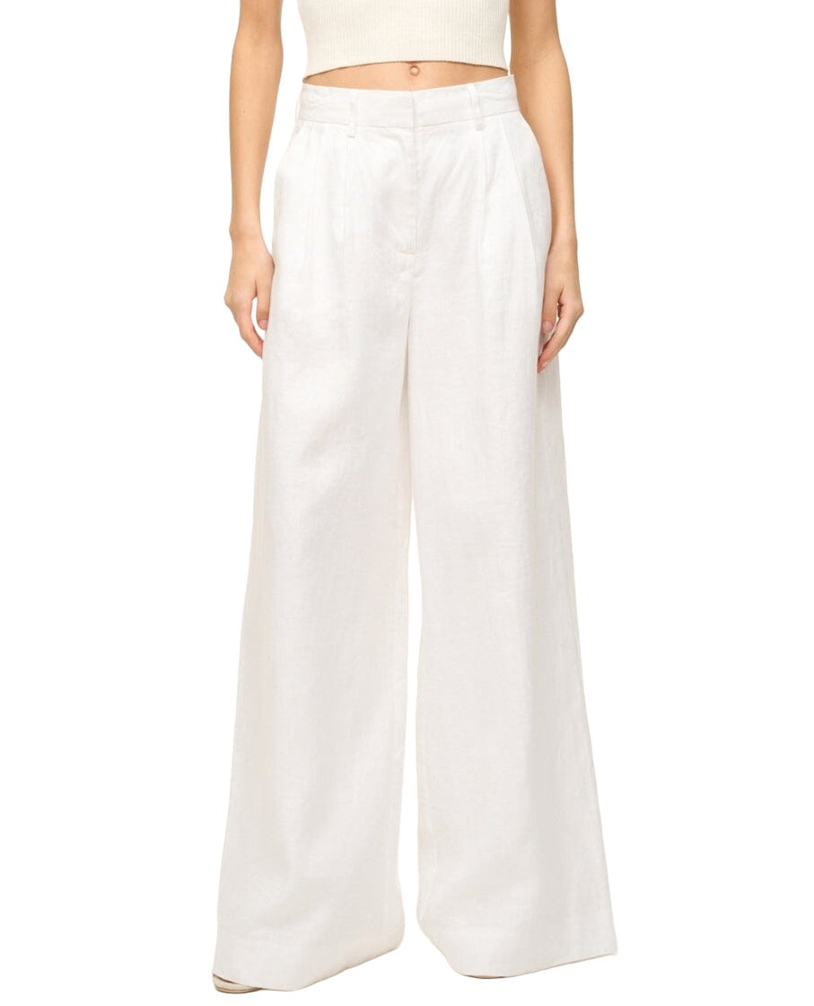 A person wearing the Staud Sasha Pant from Staud, which features high-waisted, wide-leg pleated white linen trousers with front slash pockets, paired with a cropped sleeveless top.