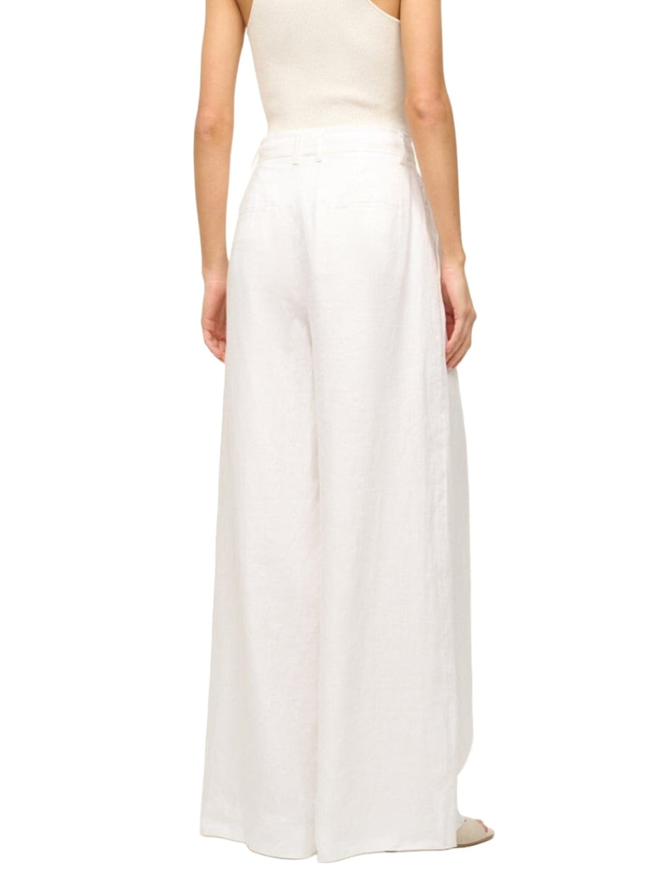 A person is shown from the back, wearing the wide-leg pleated Staud Sasha Pant in white and a sleeveless beige top.