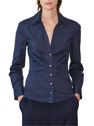A person showcases a tailored silhouette in the Callas Milano Savile Top, a fitted navy button-up made from cotton poplin, with matching pants, against a plain background. Hands rest in pockets for added style.